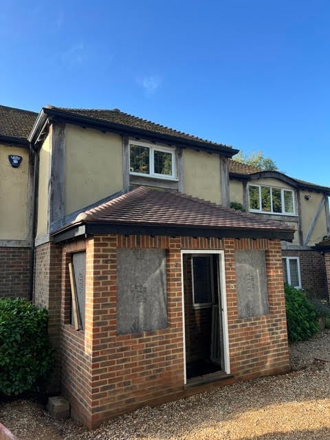 Brick extension attached to a two-story cream and dark timber-framed house with clear blue sky