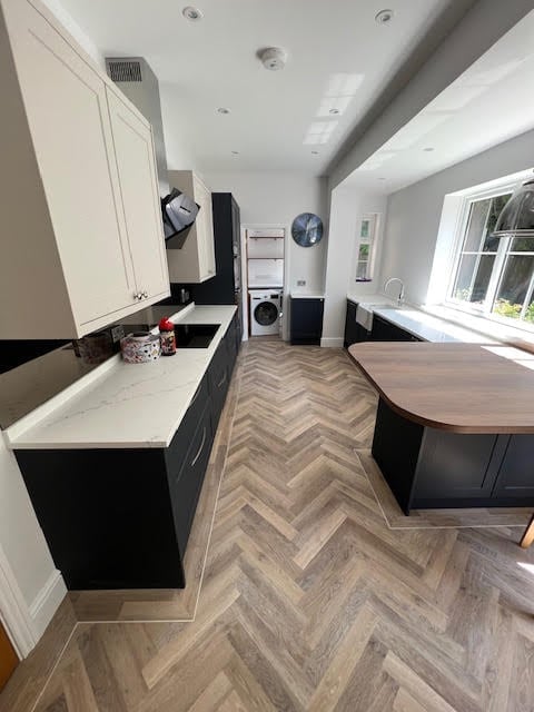 Modern kitchen with black and white cabinets, herringbone wood flooring, island counter, and natural light from window