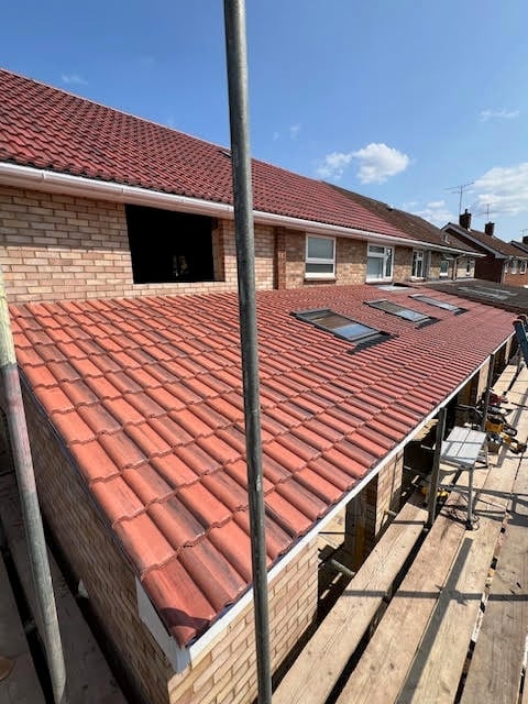 Residential roof under renovation with red clay tiles, brick walls, metal pole, and skylights during construction