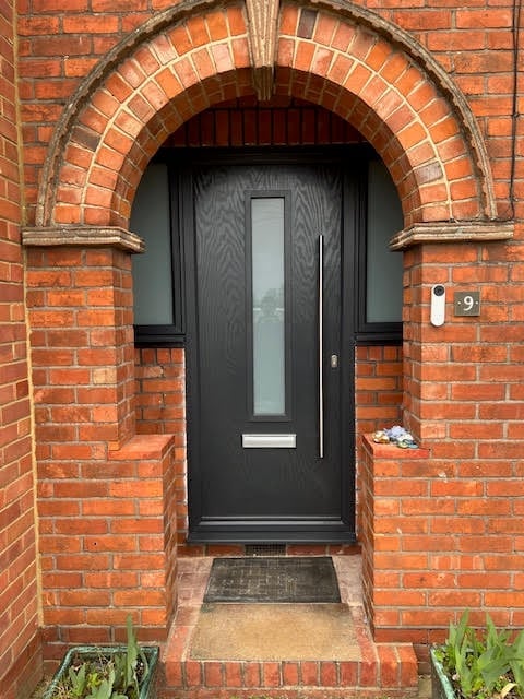 Black front door with glass panel on red brick building entrance with arched archway