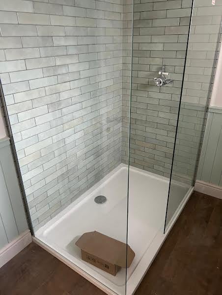 Modern glass-enclosed shower stall with white subway tile walls and white base, featuring a cardboard box on the floor