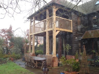 Wooden deck and porch of a rustic two-story house surrounded by bare branches and overgrown vegetation